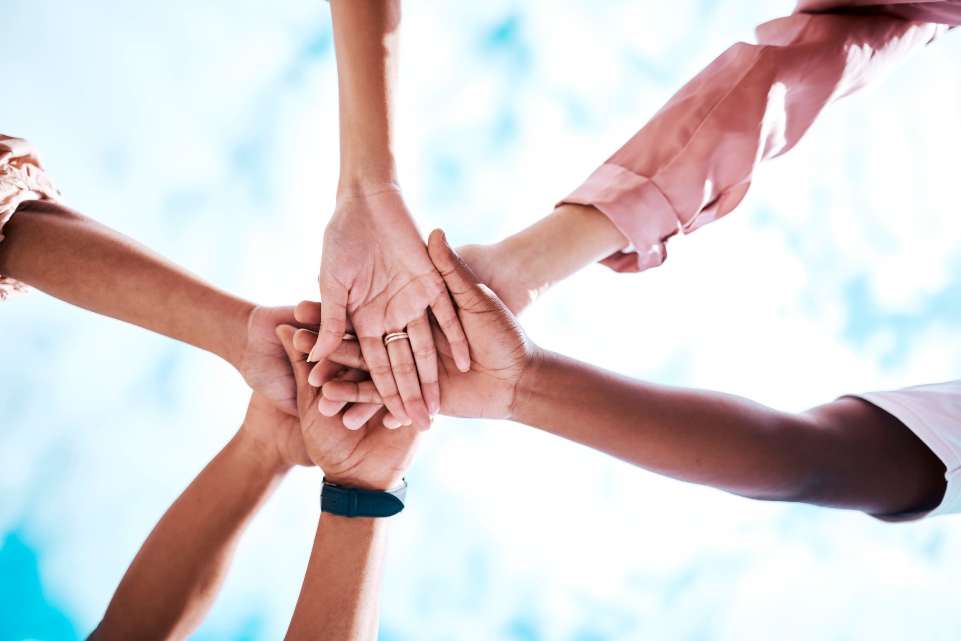 Hands stacked, motivation and team building on a blue sky for trust, community and about us. Mission, support and friends in a low huddle for success, celebration and solidarity  together as a group